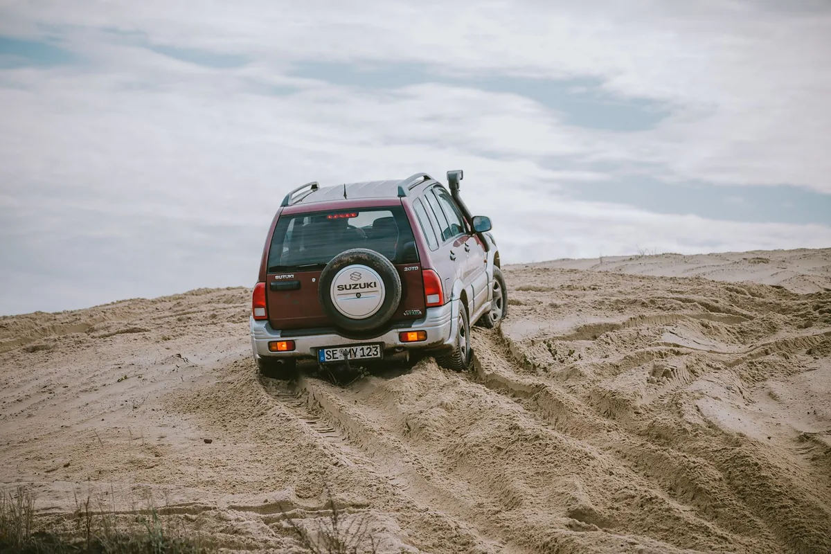 Suzuki 4x4 driving through soft sand ruts on an off-road track